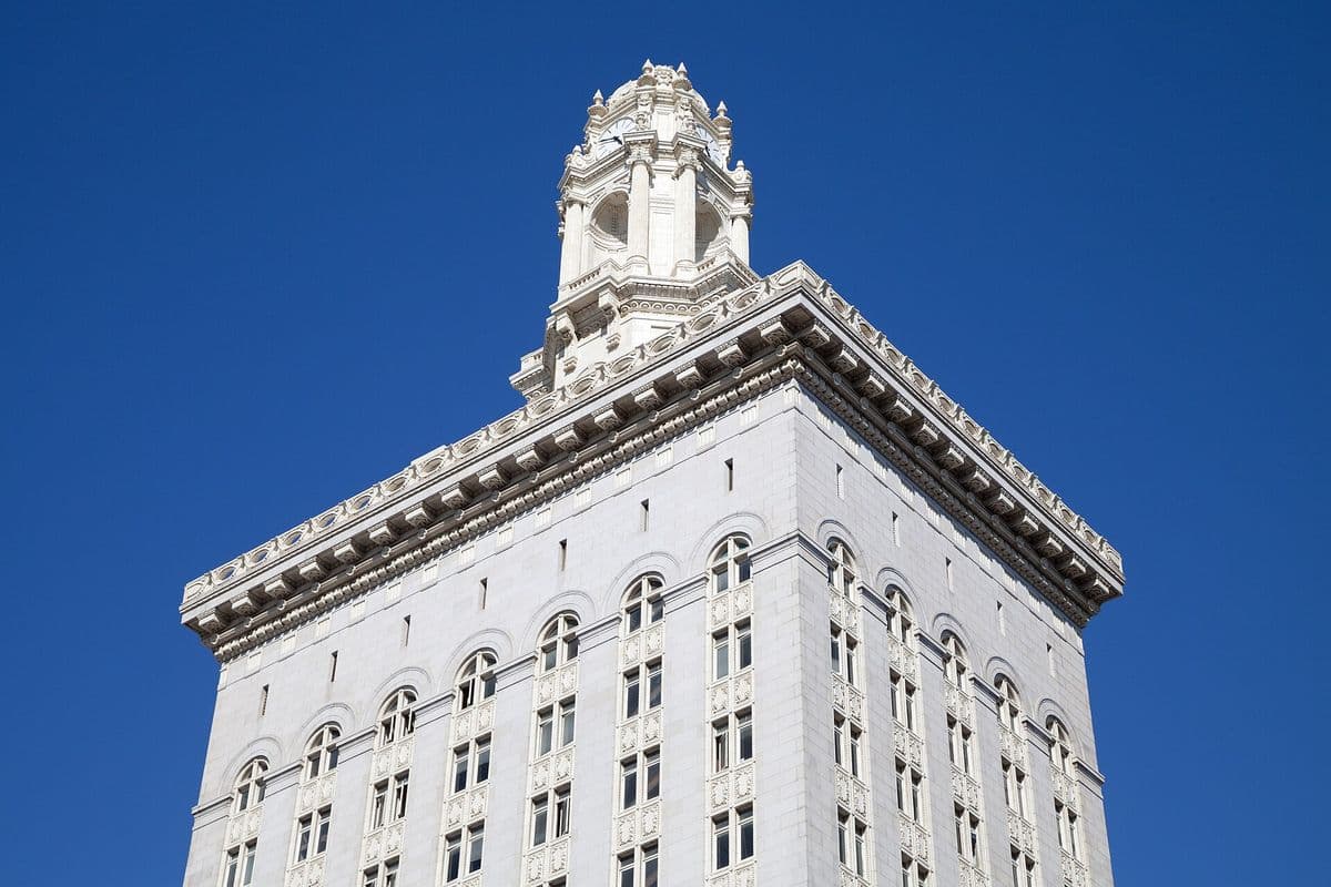 The clock tower of Oakland City Hall against a blue sky